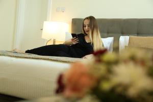 Uma mulher sentada numa cama a olhar para o telemóvel. em Uptown Hotel Apartment Fujairah By Gewan em Fujairah