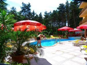 a woman standing next to a swimming pool with an umbrella at Hotel Valena in Kiten