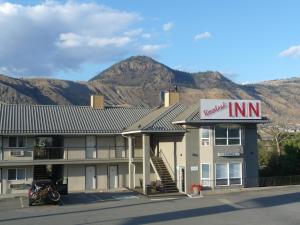 a inn with a sign on it with mountains in the background at Riverland Inn & Suites in Kamloops
