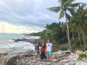 un grupo de tres personas de pie en las rocas cerca del océano en Hub of Joys Hostel en Ko Lanta