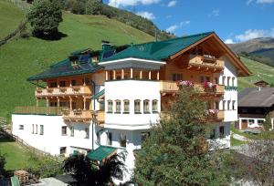 a large white building with a green roof on a hill at Hubertushof Ferienwohnungen in Gerlos