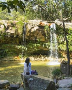 a woman sitting on a rock in front of a waterfall at Pousada Mirante das Pedras in São Thomé das Letras