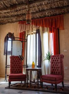 two chairs and a table in a room with windows at Shanda Lodge Desert Resort in Al Qaşr