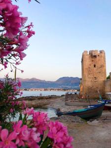 a castle and a boat on the shore with pink flowers at Stunning Sicilian Villa in Carini