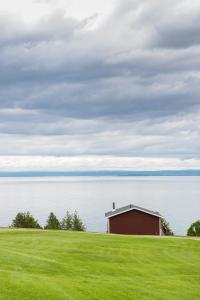 a red barn on a grassy hill next to the water at Domaine Frais Air in La Malbaie