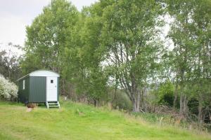 a green and white shed on a hill with trees at Howe of Torbeg in Ballater