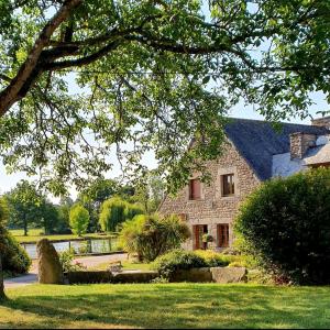 une grande maison en pierre avec un étang en face de celle-ci dans l'établissement Le Petit Moulin du Rouvre, à Saint-Pierre-de-Plesguen