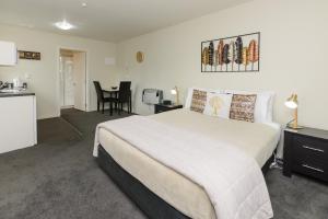 a bedroom with a large white bed and a kitchen at Ellena Court Motel in Blenheim