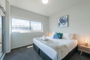 a white bedroom with a bed and a window at Astra Apartments Newcastle (Merewether) in Merewether