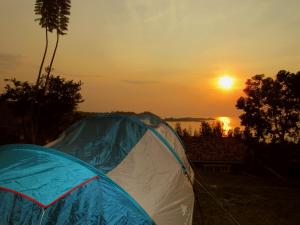 ein blau-weißes Zelt mit Sonnenuntergang im Hintergrund in der Unterkunft Rebero Kivu Resort in Kibuye