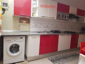 eine Küche mit roten und weißen Schränken und einer Waschmaschine in der Unterkunft APPARTEMENT "NESRINE" Kélibia in Kelibia