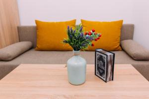 un jarrón blanco con flores en una mesa junto a un libro en Apart-hotel on Kondrateva street New Building, en Sumy