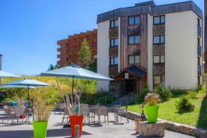 ein Hotel mit Tischen und Sonnenschirmen vor einem Gebäude in der Unterkunft VTF Le Balcon de l'Alpe in L'Alpe-d'Huez