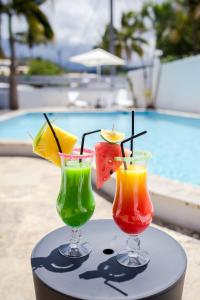 three colorful cocktails sitting on a table next to a pool at Appartements Le Bleu des Roches Noires in Saint-Gilles-les-Bains