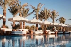 a pool with chairs and umbrellas and palm trees at Nikki Beach Resort & Spa Santorini in Kamari
