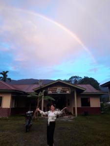 a woman standing in front of a house with a rainbow at Mulu D cave homestay in Mulu