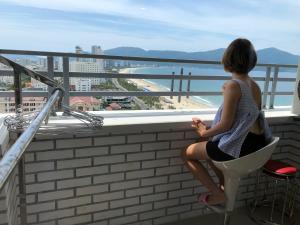 a woman sitting in a chair on a balcony looking at the ocean at My Khe beach apartment hotel, 2 bedrooms in Da Nang