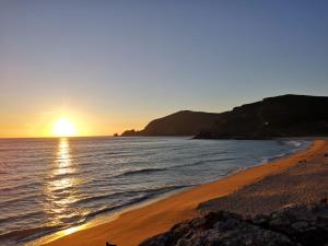 a beach with the sun setting over the ocean at Albergue Por Fin in Fisterra