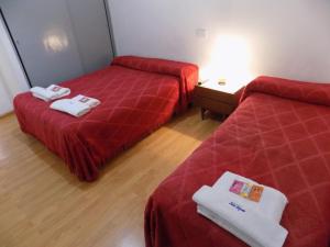 2 camas en una habitación con sábanas rojas y toallas en Hotel Belgrano en Perito Moreno