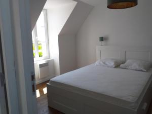 a white bed in a white room with a window at LA ROLANDE in Penmarch