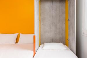 two beds in a room with an orange wall at ibis budget Lyon Est Beynost in Beynost