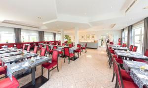 ein Restaurant mit Holztischen und roten Stühlen in der Unterkunft Hotel Alarun Munich by Mayburgh in Unterschleißheim