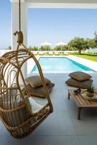una sedia in rattan appesa accanto alla piscina di Vilana White Elegant Villa a Roúpai
