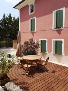 eine Holzterrasse mit einem Tisch und Stühlen sowie ein rosafarbenes Haus in der Unterkunft La Bastide du Limon in Mormoiron
