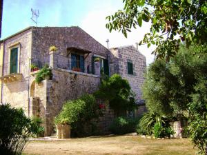 Casa de piedra antigua con balcón y árboles en Liolà, en Módica