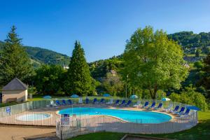 une grande piscine avec des chaises et des arbres bleus dans l'établissement Résidence Goélia Les Gorges de la Truyère, à Entraygues-sur-Truyère