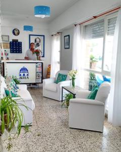a living room with white furniture and a man in the kitchen at Hostería Altea in Monte Hermoso