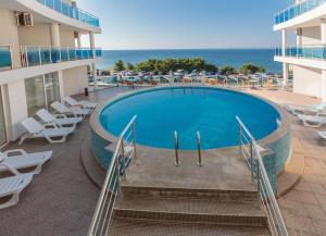 a swimming pool next to a building with chairs and the ocean at DEA Pasavan Apartments in Ravda