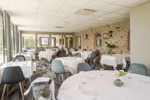 un restaurant avec des tables blanches, des chaises et des fenêtres dans l'établissement Au Relais Du Gué De Selle, à Évron