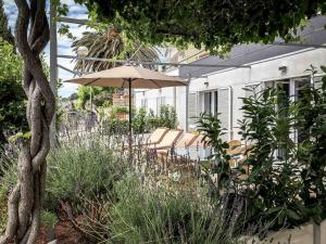eine Terrasse mit Stühlen und einem Sonnenschirm in einem Garten in der Unterkunft Apartments Melani Hvar in Hvar