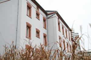 un bâtiment blanc avec des fenêtres marron et de l'herbe haute dans l'établissement ALCATRAZ Hotel am Japanischen Garten, à Kaiserslautern