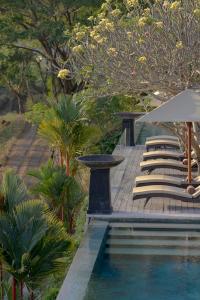 a swimming pool with lounge chairs and an umbrella at The Puncak Lombok in Senggigi