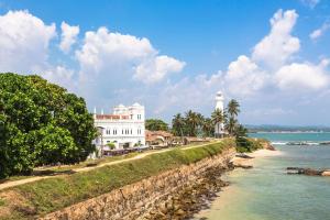 a white building next to the water with a lighthouse at Nisala Guest in Galle