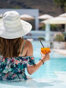 Una donna con un cappello che regge un drink in piscina di Aurora Luxury Suites a Imerovigli