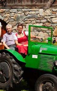 Un uomo e una donna in piedi accanto a un trattore verde di Gasthof zur Schmiede a Berg im Drautal