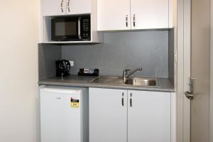 a kitchen with white cabinets and a sink and a microwave at Reef Gardens Motel in Proserpine