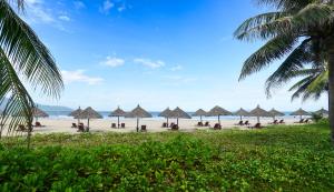 a beach with many straw umbrellas and the ocean at Furama Villas Danang in Danang