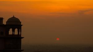 a sunset with a tower and a red sun in the sky at Neemrana's - Tijara Fort Palace in Alwar