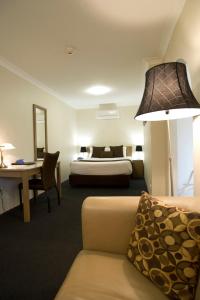 a hotel room with a bed and a couch and a lamp at Noah's Mid City Motor Inn Muswellbrook in Muswellbrook