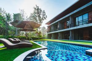 a swimming pool with chairs and an umbrella next to a building at Stucco Loft Residency in Chiang Mai
