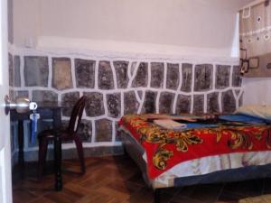 1 dormitorio con pared de piedra, cama y silla en Casa LLEMO, en San Pedro La Laguna