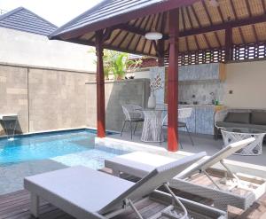 a pool with chairs and a table and an umbrella at Theanna Villa and Spa Canggu in Canggu