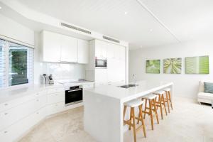 a kitchen with white cabinets and a kitchen island with bar stools at Allambi Apartment 1, 25 Allambi Rise, Little Cove in Noosa Heads