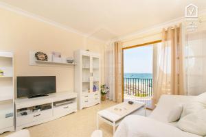 a white living room with a television and a balcony at E142 Carabela Beach by Mallorca Villa Selection in Alcudia