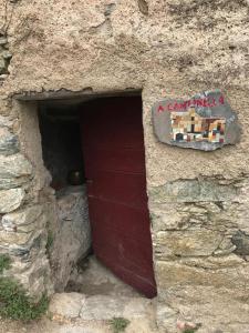 - un bâtiment en pierre avec une porte rouge et un panneau dans l'établissement ,A cantinella, une cave a fromage au centre corse, à Santa-Lucia-di-Mercurio