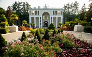 a garden in front of a white house with flowers at RODINA Grand Hotel & SPA in Sochi